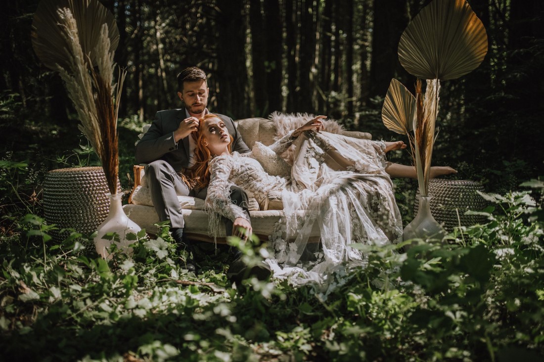 Newlyweds kiss and lounge on beige settee in the forest surrounded by pampas grass