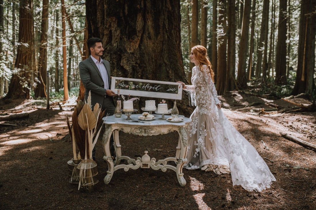 Newlyweds hold sign over their forest dessert table