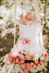 White wedding cake with pink flowers hangs out of tree in Vancouver Island forest