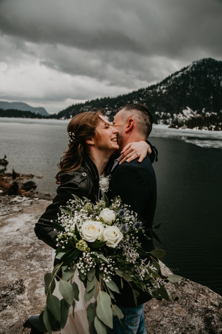 Newlyweds embrace by mountain top lake in BC
