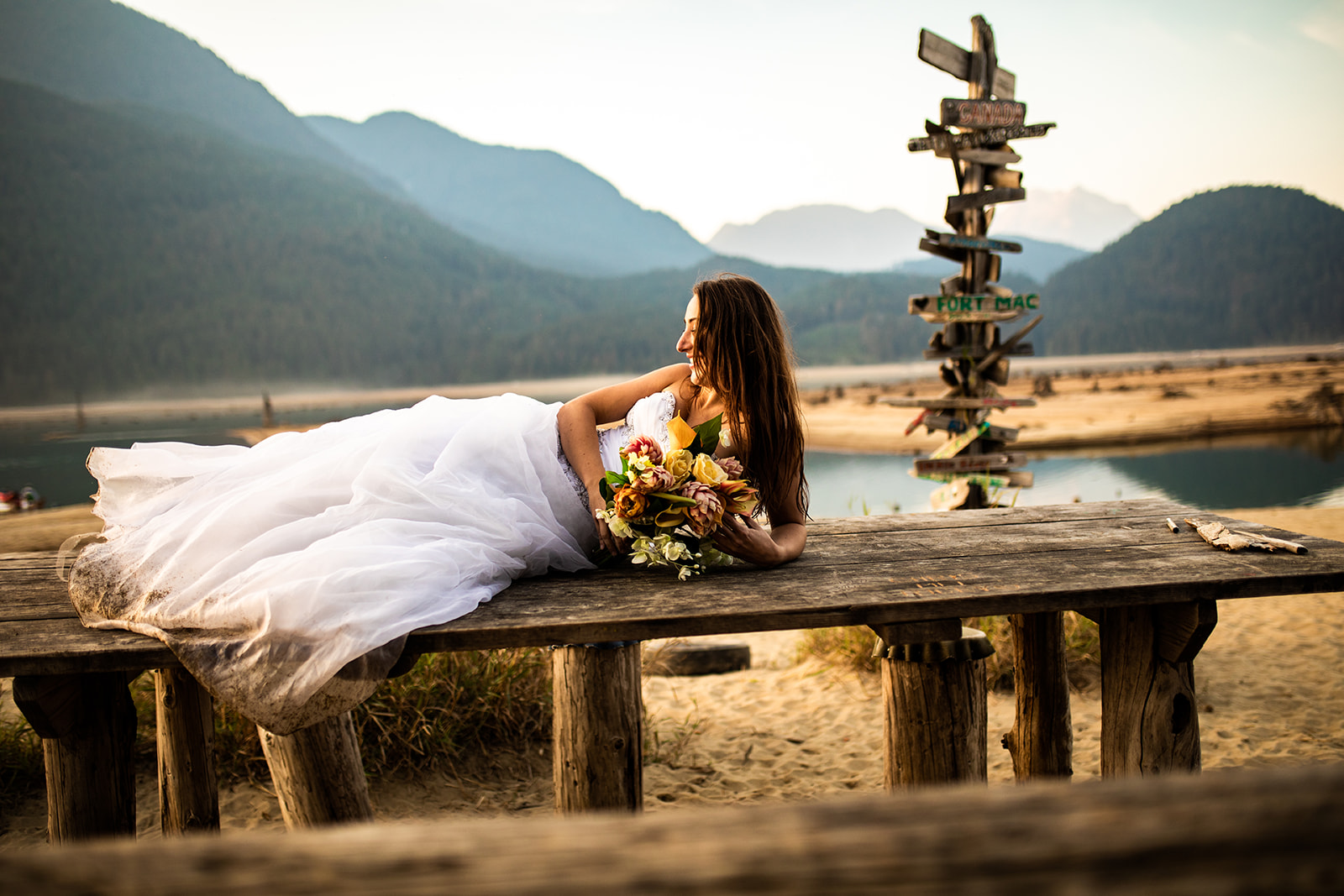 Bride lays on railing looking out at Vancouver Lake