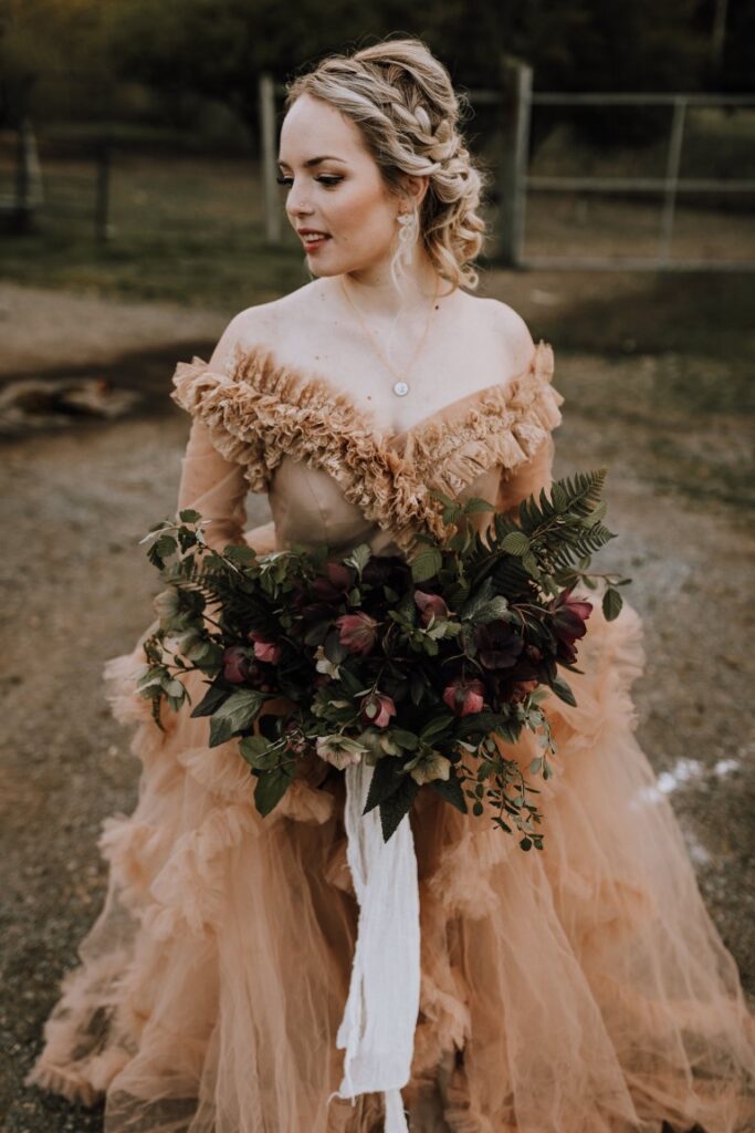 Bride'in peach gown holds bouquet of greenery and white and red flowers