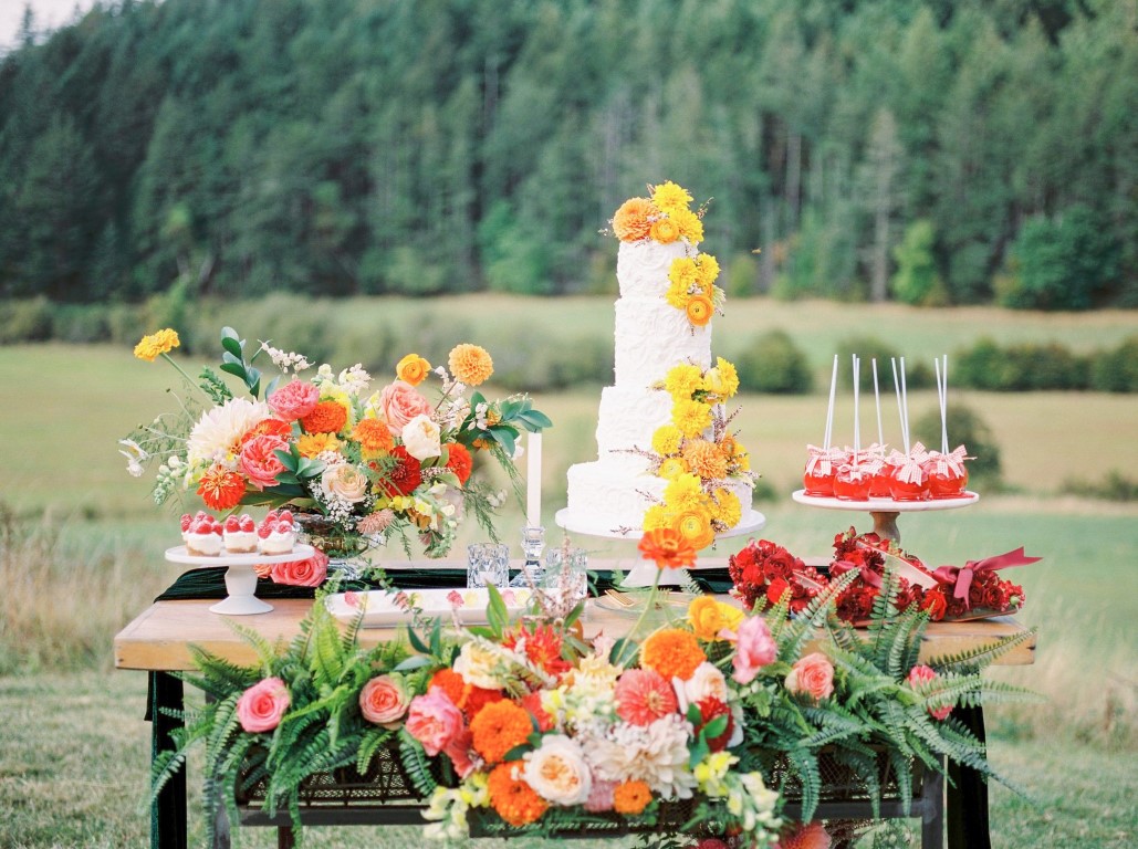 Somewhere Over The. Rainbow Cake Table with bright flowers sitting in a field