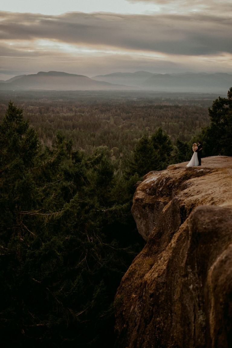 Bride and groom stand on rock outcrop on Vancouver Island