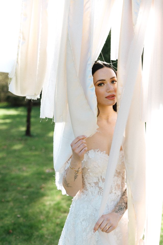 tattooed bride in modern white lace gown off-the-shoulder gown peeks through fabric detail on wood arch