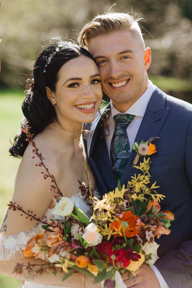 bride and groom smiling in posed portrait holding colourful floral bouquet