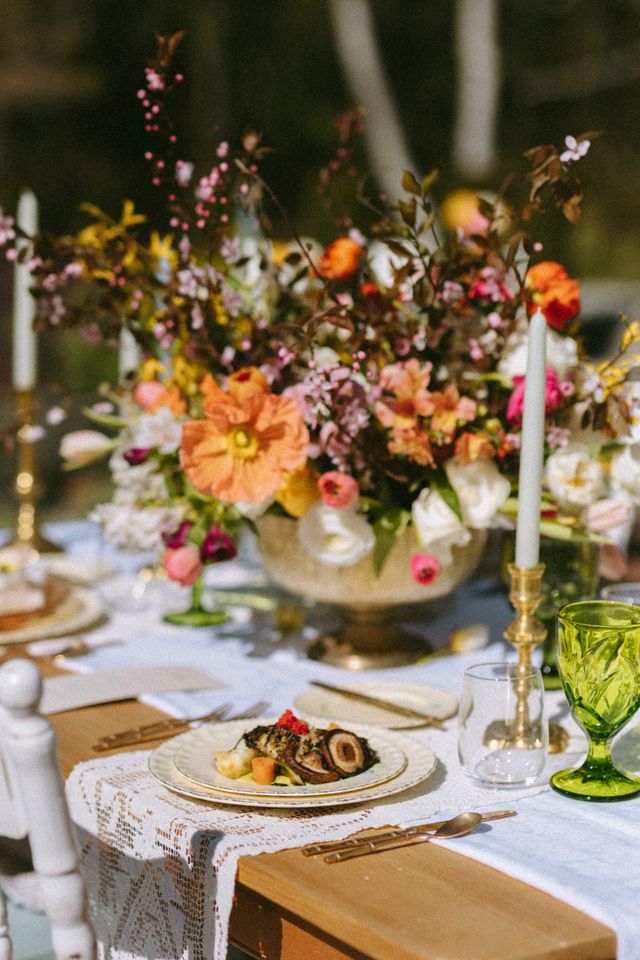 colorful floral centerpiece on table with green glassware and China table settings