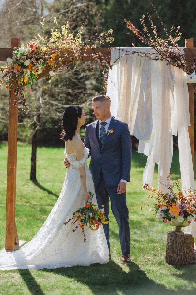 Bride and groom standing in front of wooden floral arch with fabric piece detail