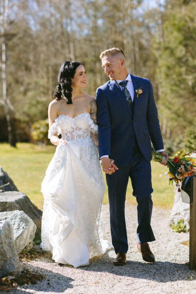 modern tattooed bride in off-the-shoulder lace gown and groom walk hand in hand with groom holding the bridal bouquet