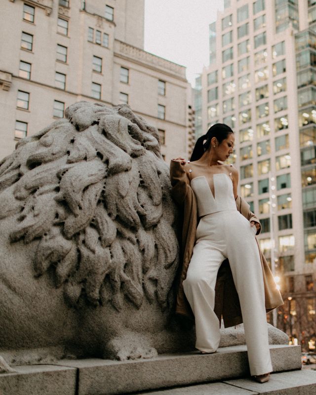 bride poses on steps with cement lion in deep plunge 2 piece couture jump suit