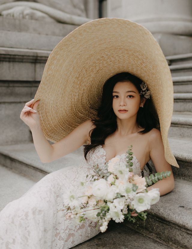 bride holds the oversized brimless hat with one hand and a white and pink floral bouquet in other