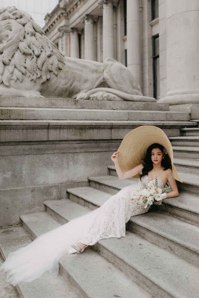 bride leans back on stairs wearing an oversized hat and holding floral bouquet