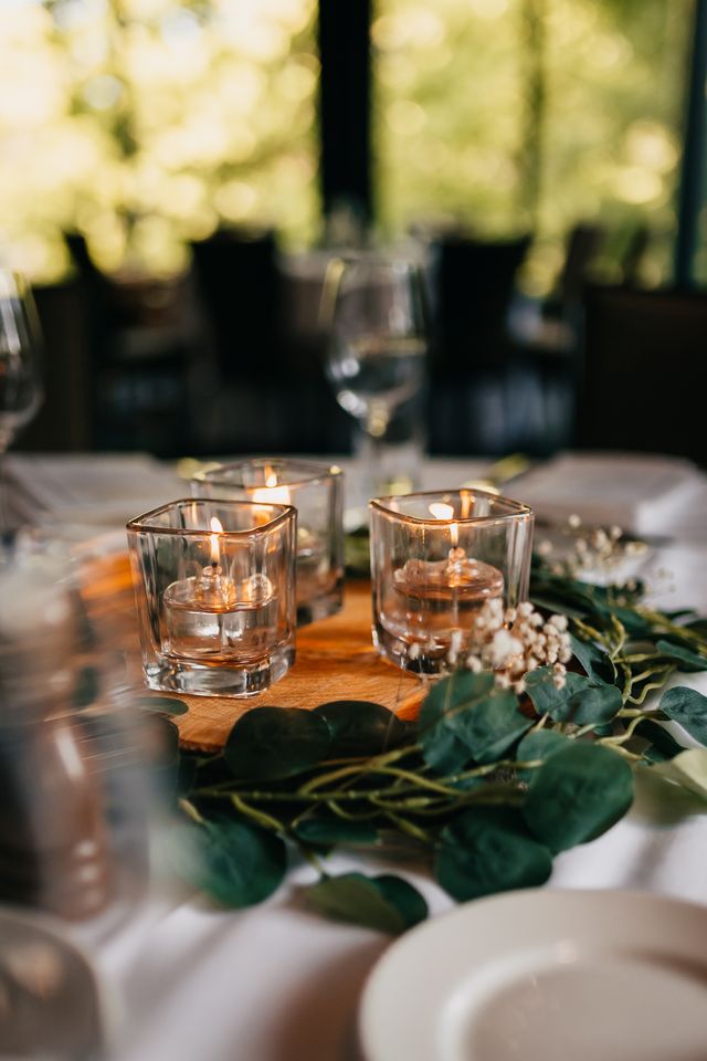 lit volitive candles on wood round amongst green leaves garland on table