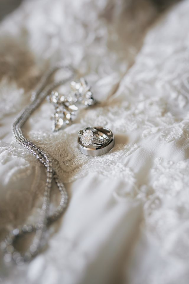 wedding band and oval engagement ring and necklace displayed on wedding dress