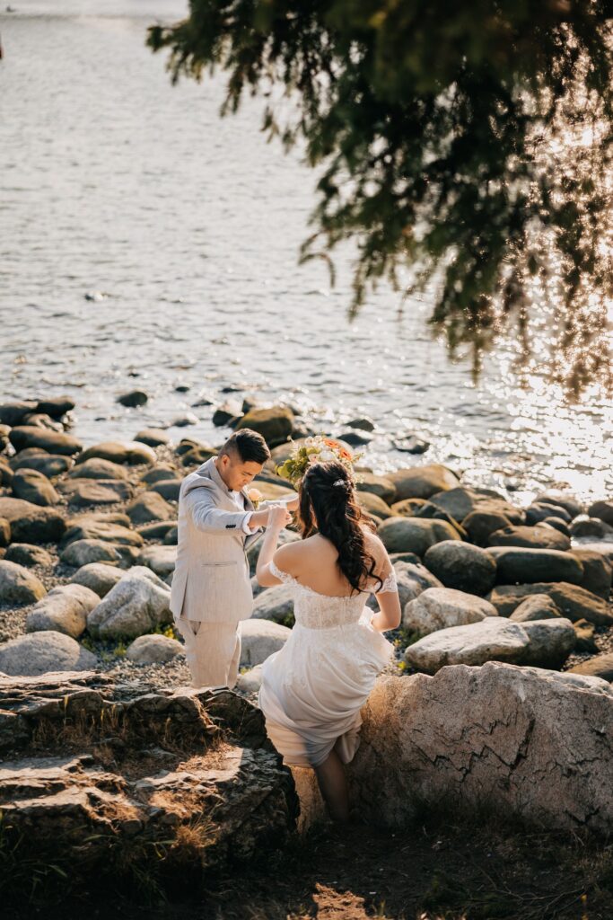 Groom helps bride down rocky beach