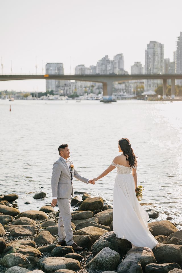 looking at each other whilst holding hands on the rocky beach, city in background