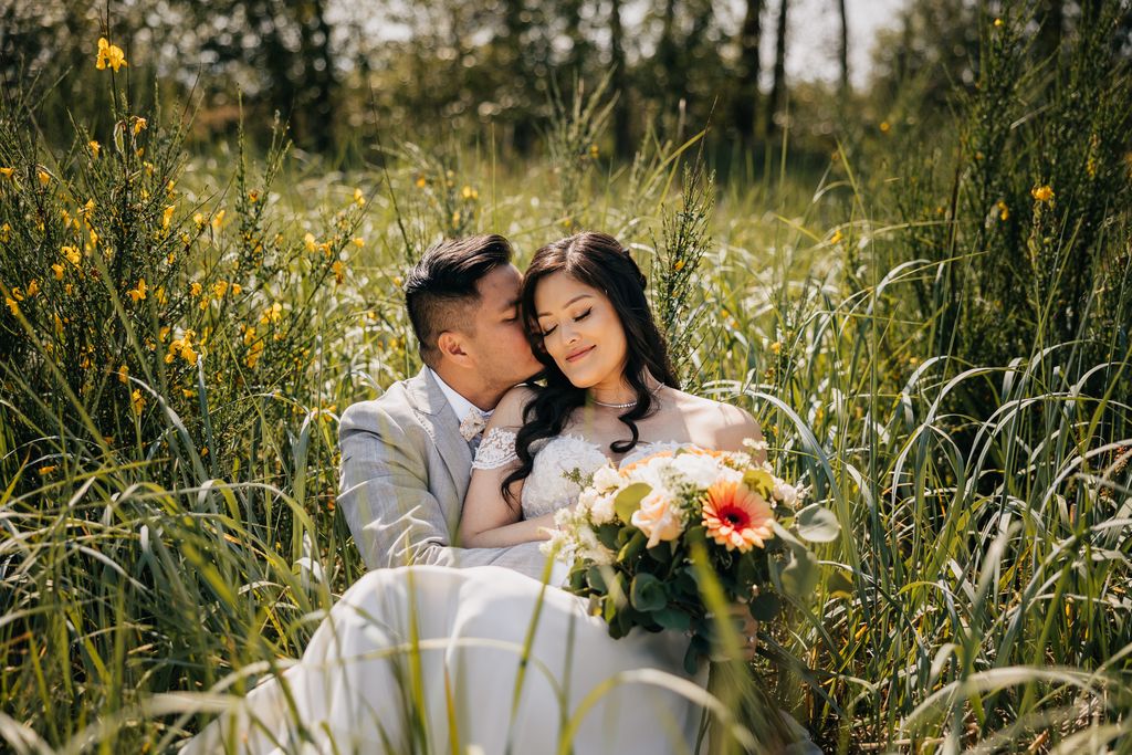 newlywed snuggles in grass, groom nuzzles into bride's hair