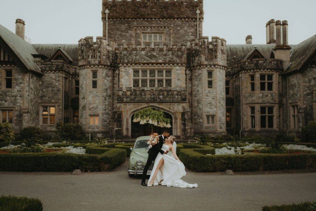 groom dips bride in front of green grey vintage car and English garden maze at hatley castle