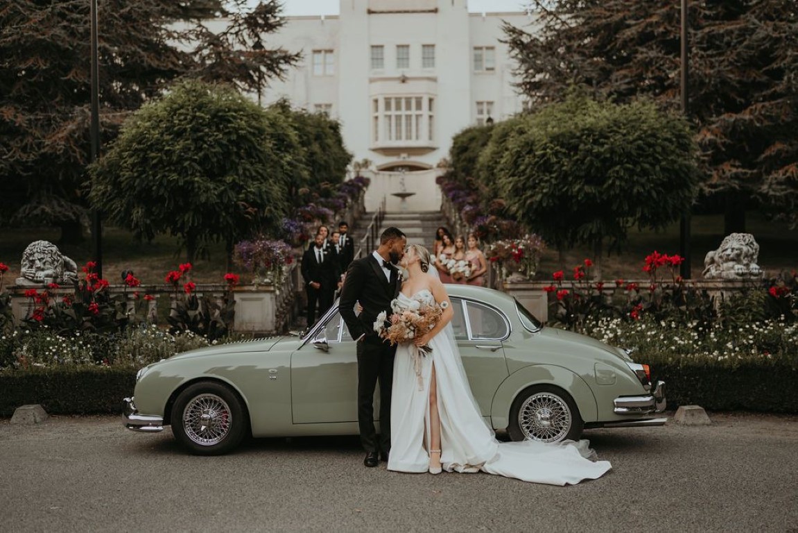 bride and groom share kiss in front of vintage classic car outside of Hatley castle at base of the grand steps