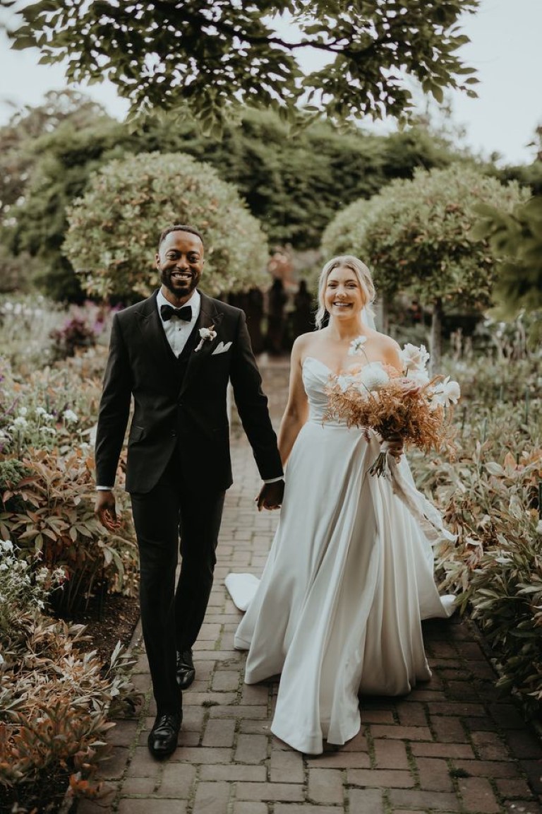 bride and groom walk hand in hand on brick walkway in castle garden