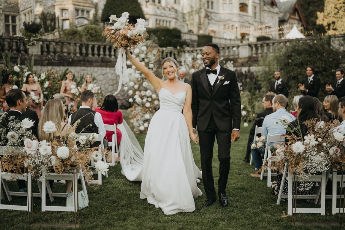 bride holds her bouquet up in air as she walks hand in hand with groom after the outdoor ceremony