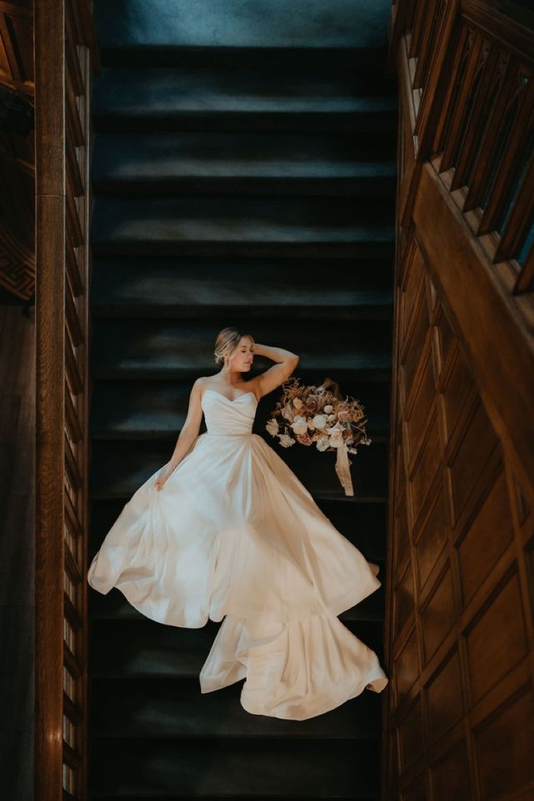 bride lays on staircase with her bridal bouquet beside her for an artsy shot from above