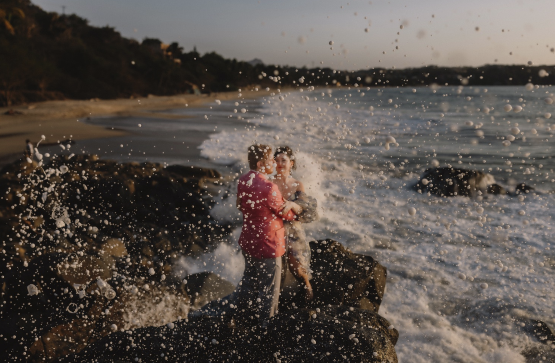 Newlyweds stand along ocean waves by Gable McClintock Photography