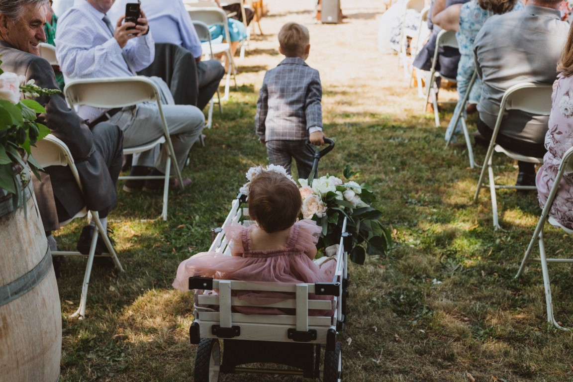 ring bearer pulls flower girl in wagon down the outdoor aisle