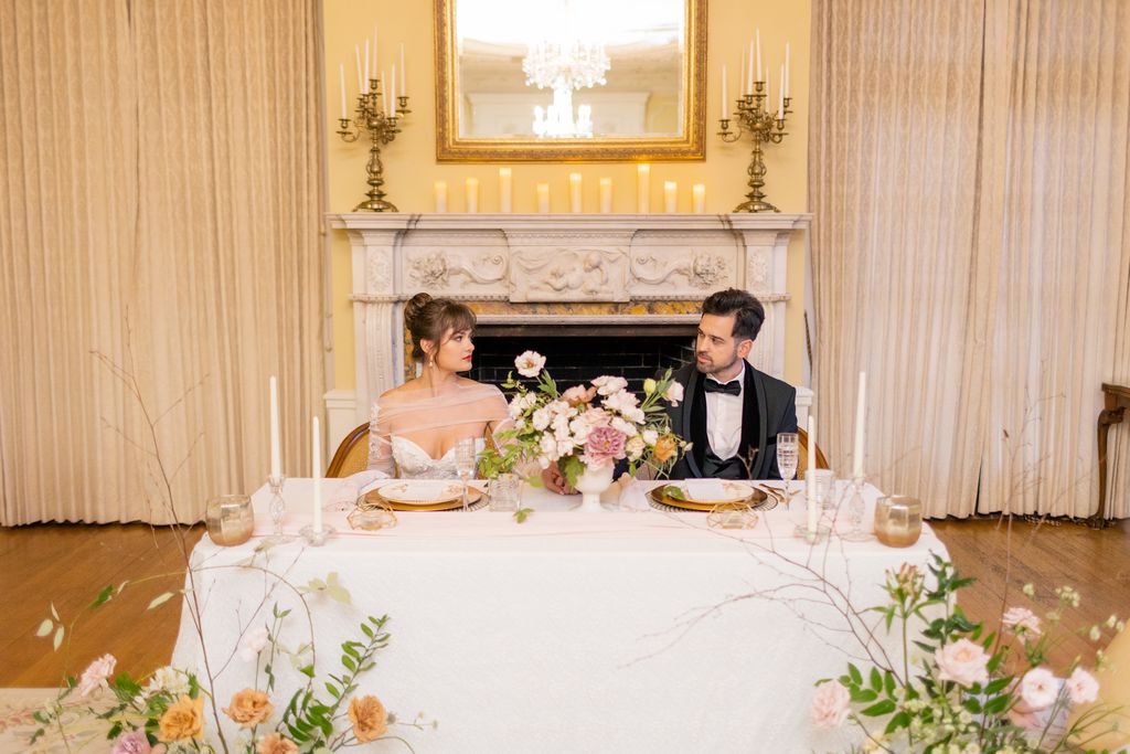 couple sits together at sweetheart table with white linens and gold plates