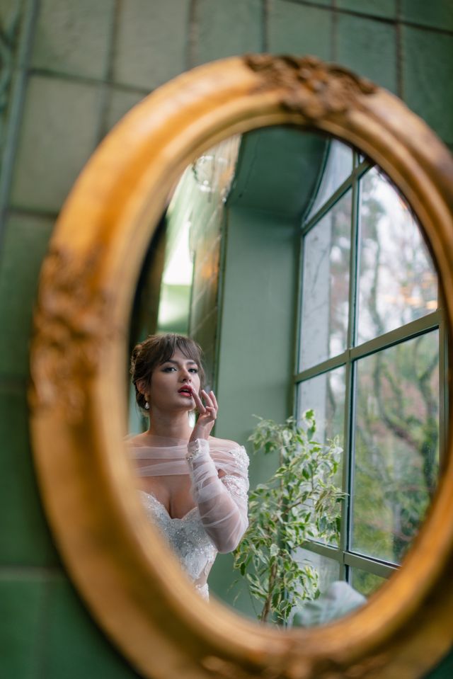 bride checks her makeup in a large ornate oval mirror