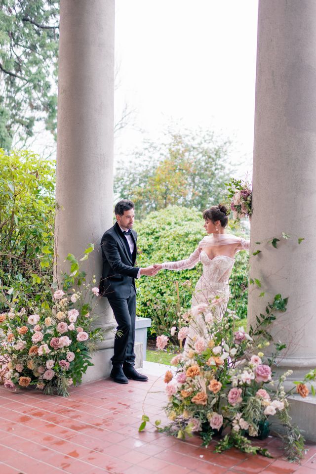 bride and groom hold hands around pillars and large florals and greenery