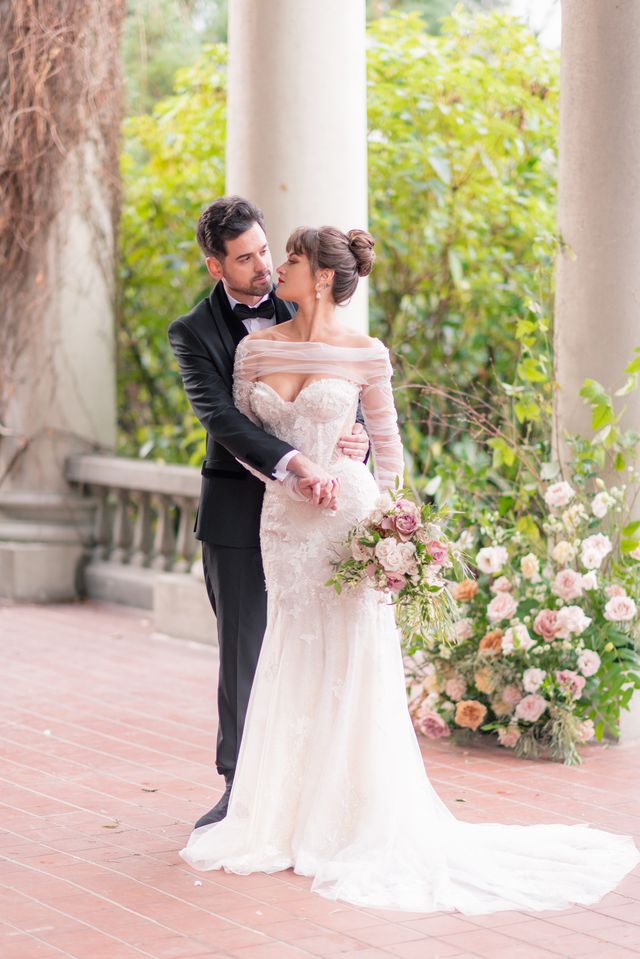 newlyweds pose for portrait on veranda by large rose floral centerpiece