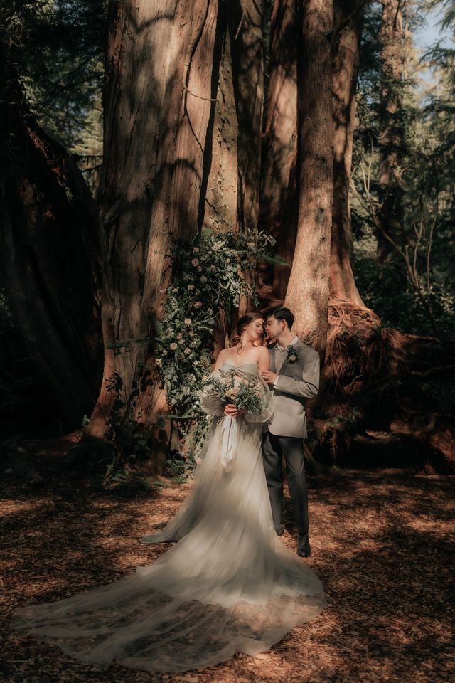 bride and groom pose in front of tree with large florals in background