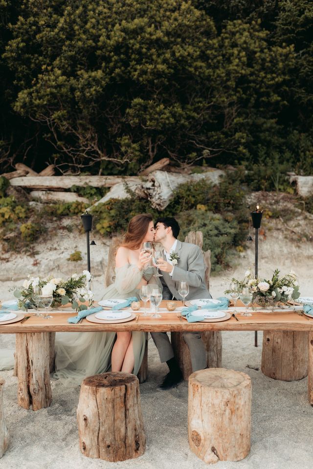 bride and groom share kiss whilst sitting at outdoor table