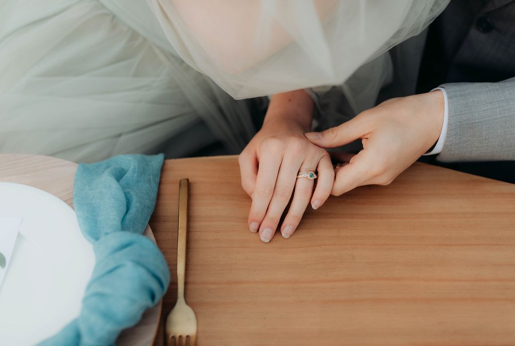 groom holds bride's hand at table