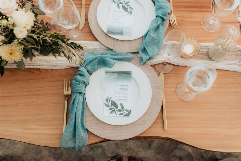 curvy wood table with wood chargers and gold cutlery