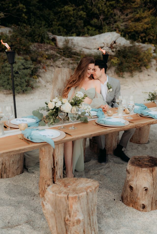 couple sit on wood stumps at rustic beach table