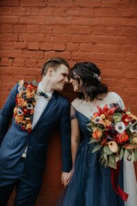 Bride and groom against red brick wall by LumiPhoto