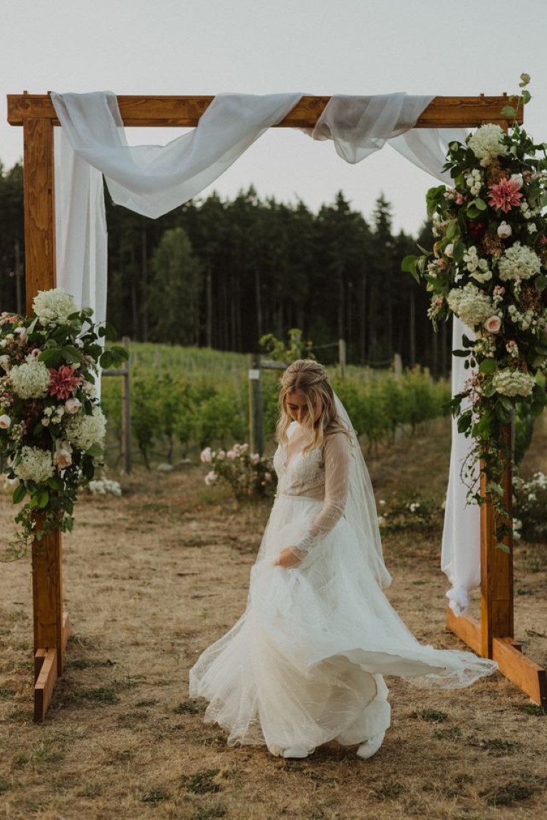 bride twirls under her wooden arch with draping fabric and large floral displays on either side