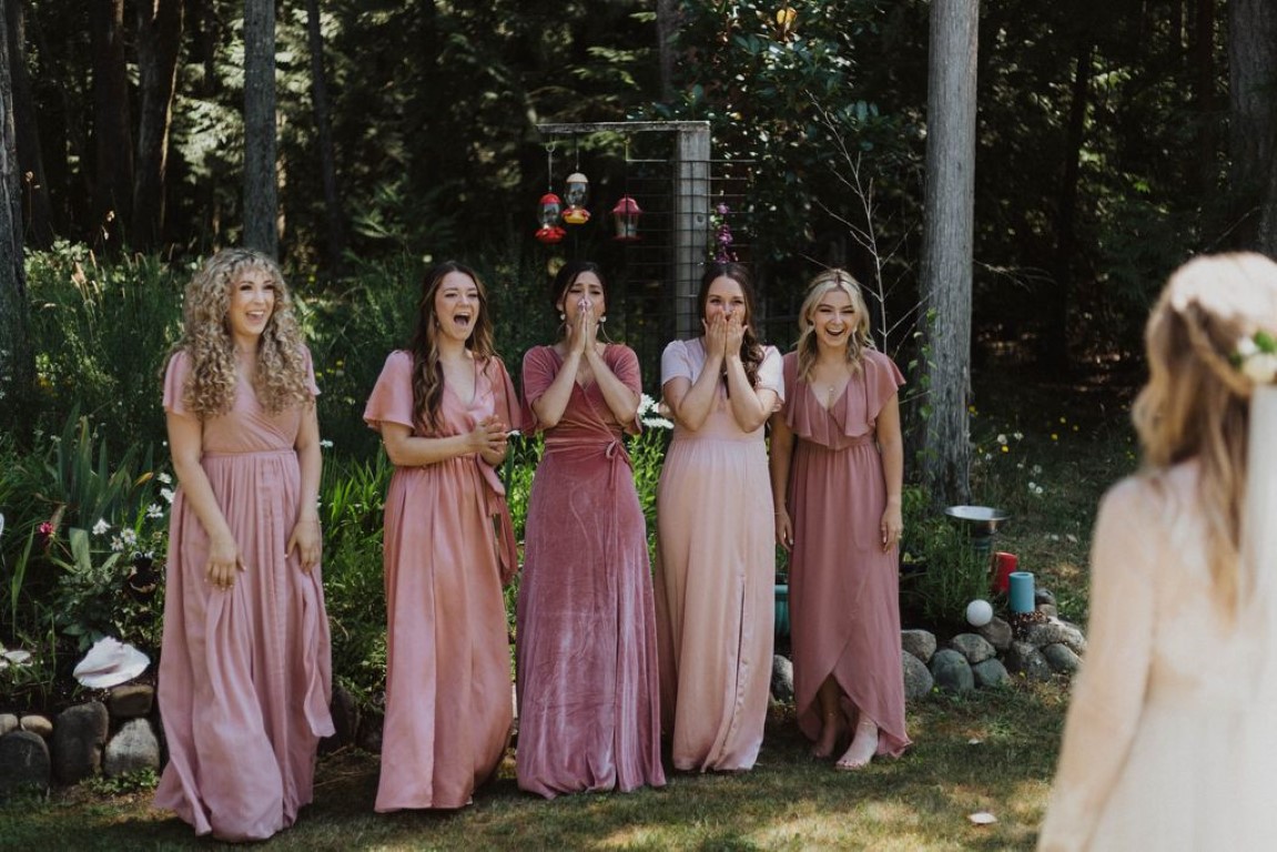 bride has first look with bridesmaids all wearing dresses in various shades of pink