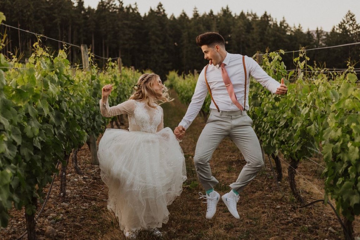 playful bride and groom jump for joy in the vineyard of Vancouver Island winery