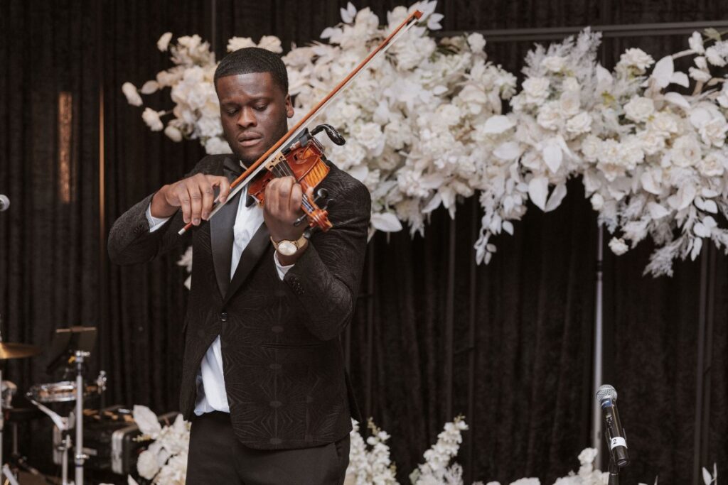 violin player LordNation in front of white floral design at West Coast Wedding Show Vancouver