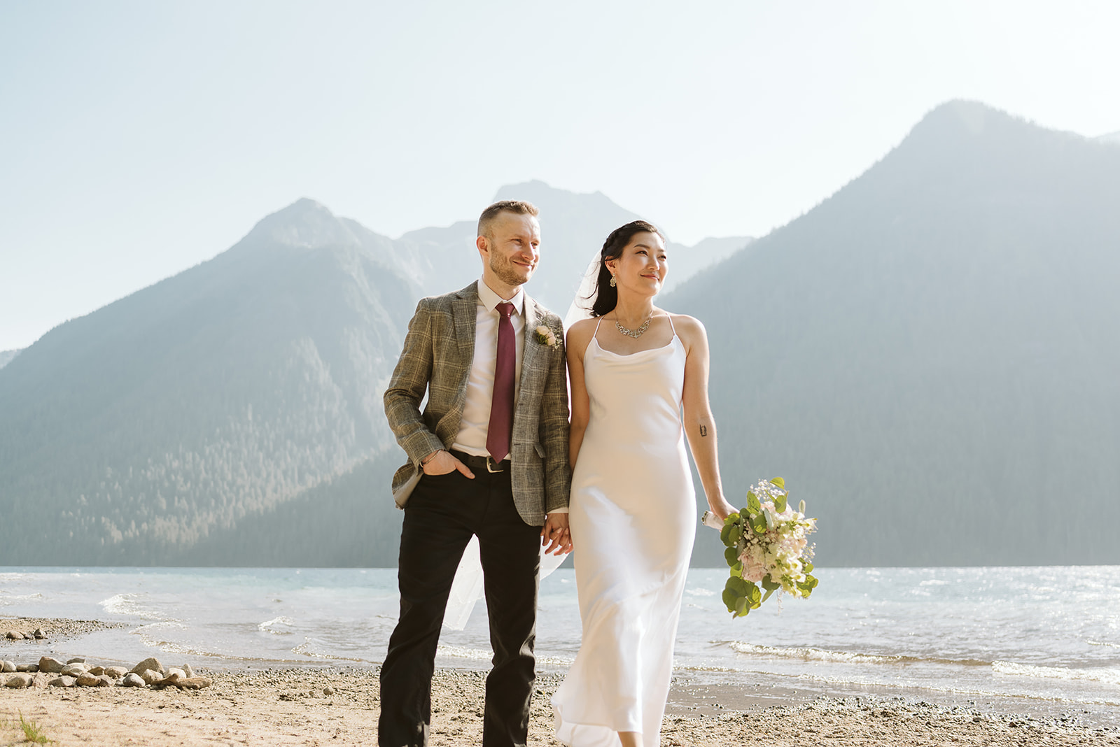 Bride and groom walk beside mountain lake in BC