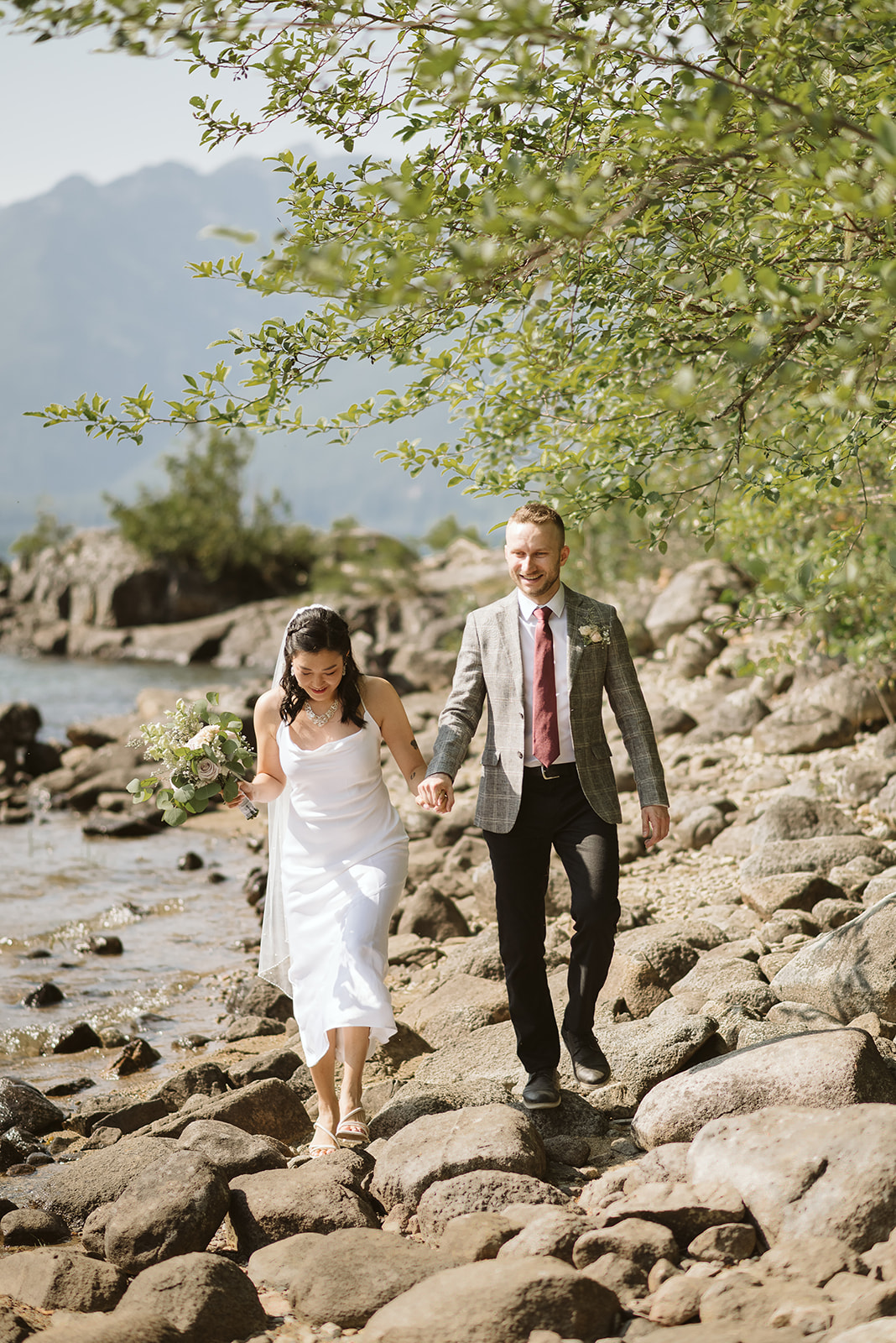 Wedding couple walks along mountain lake towards ceremony