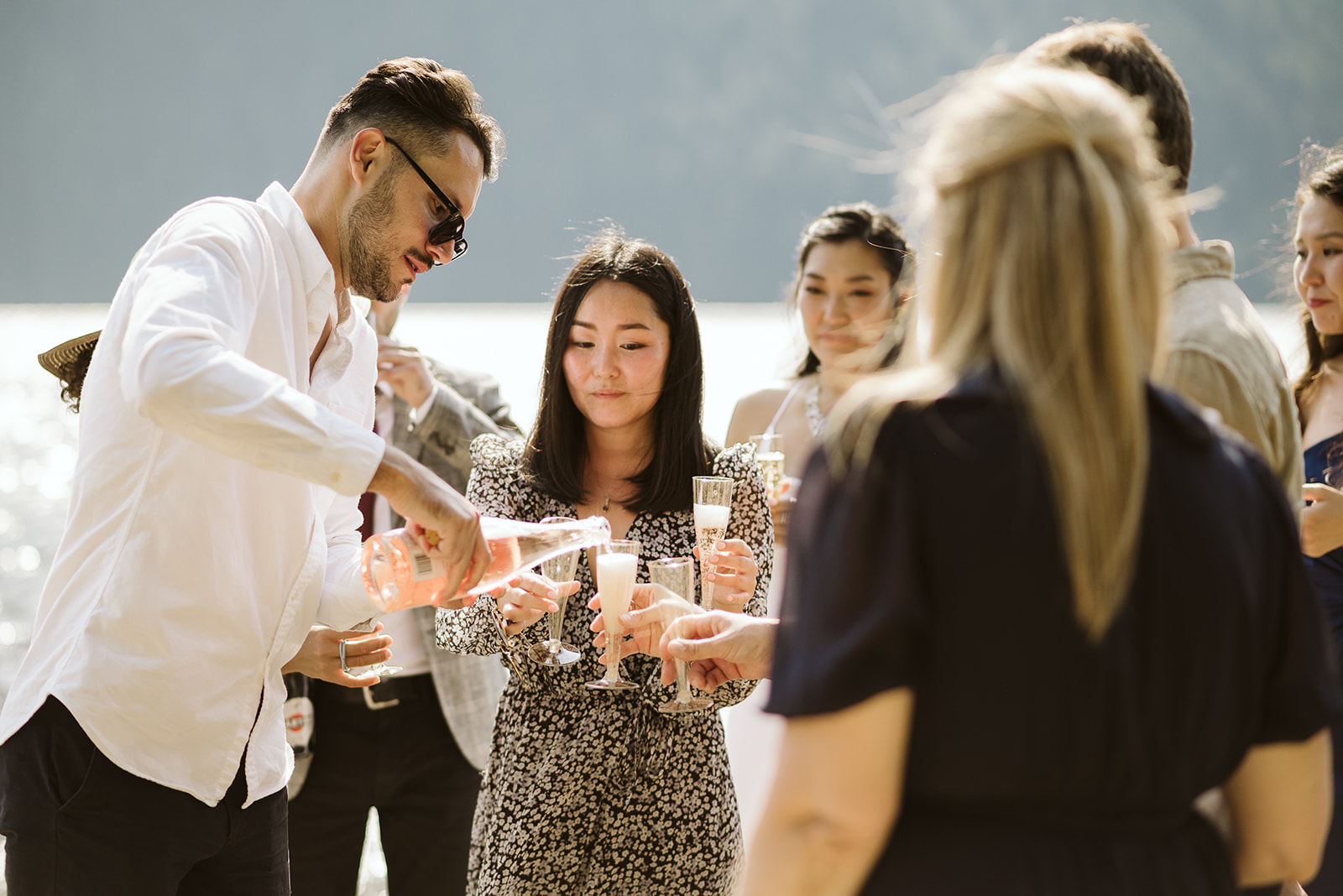 Guests pour champagne to celebrate mountain lake wedding