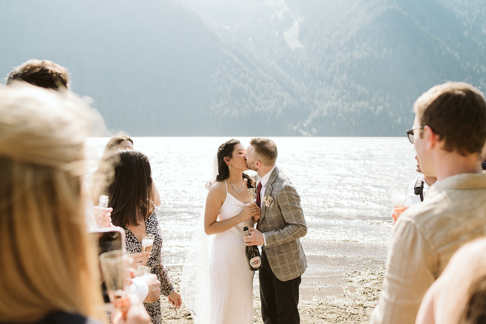 Newlyweds kiss in front of mountain lake