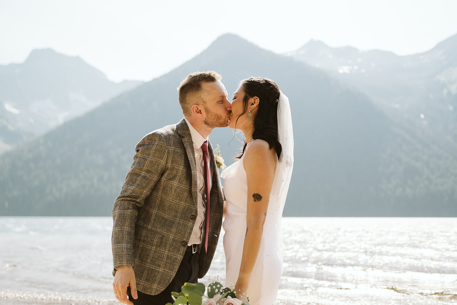 Newlyweds kissing with mountains behind