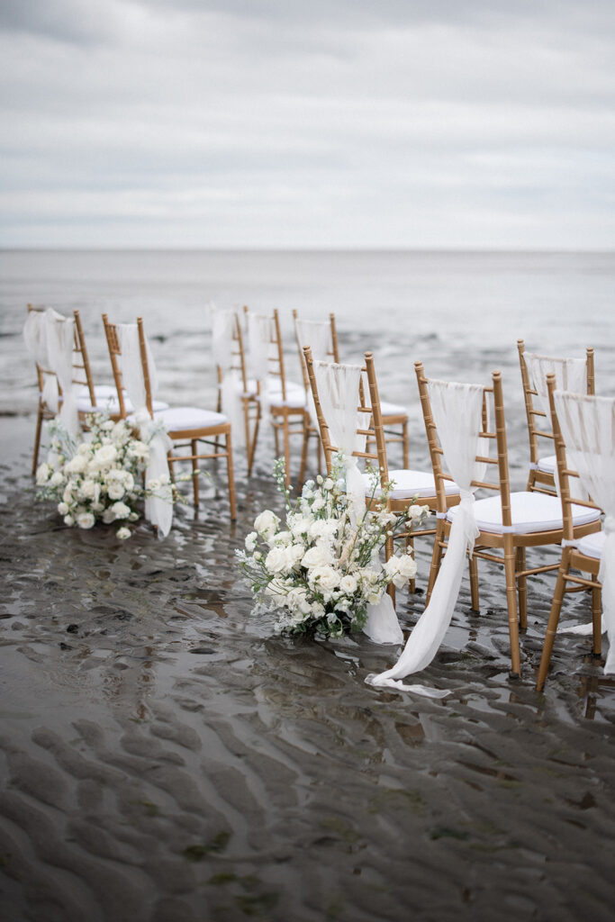 gold Chiavari chairs with white fabric and roses sit on Vancouver beach