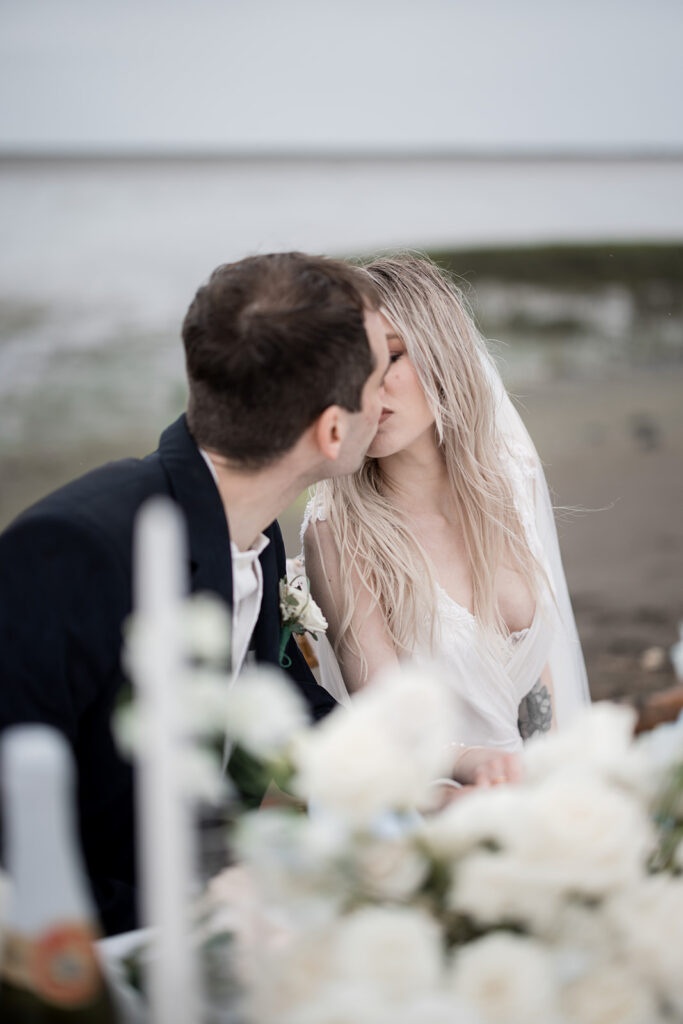 Newlyweds kiss at beach sweetheart table in Vancouver