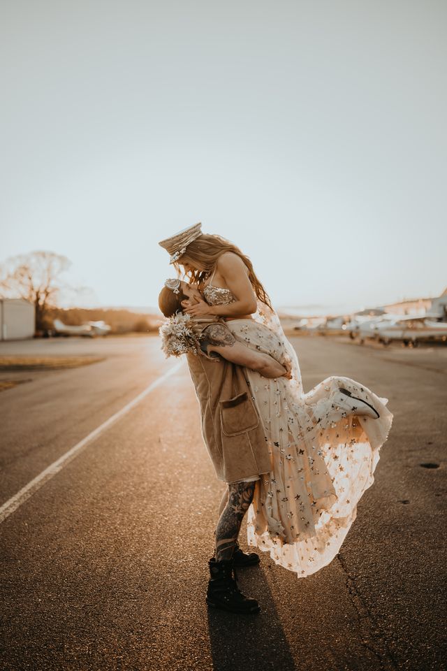 Groom lifts bride up on airport runway